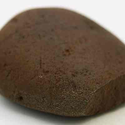 Closeup of basalt hammerstone: The image shows a close-up of a smooth, brown rock with a slightly flattened side, resting on a plain white surface.