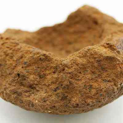 Closeup profile of broken cup or mortar base: The image shows a weathered, rust-brown, stone-like cup or mortar with an irregular shape.