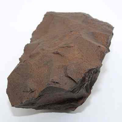 Basalt adze blank: The image shows a rough, angular piece of reddish-brown rock with visible texture and jagged edges against a plain white background.