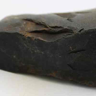 Profile of basalt adze fragment: The image shows a dark, rugged fragment of an ancient adze with noticeable weathering and textured surface, showcasing historical craftsmanship.