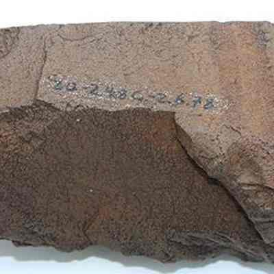 Basalt adze blank with visibile alternate id number: The image shows a large, rough brown rock, possibly an adze blank with some numbers hand-written on its surface, set against a plain white background for emphasis.