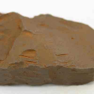 Closeup of an adze (ko'i) fragment: The image shows a rough, brown adze (ko'i) fragment with an irregular, jagged surface, placed on a white background, highlighting its rugged texture and natural appearance.