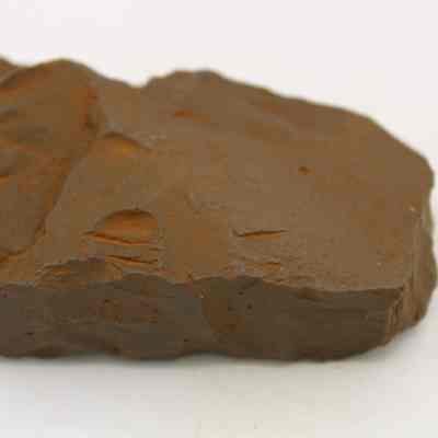 Adze (ko'i) fragment: The image shows a brown, rough-textured piece of rock adze (ko'i) fragment with an uneven surface, resting on a plain white background.
