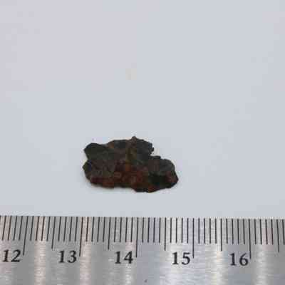 Closeup of basaltic glass flake and ruler: A small flake of basaltic glass rests beside a ruler, measuring approximately 3.5 centimeters, displaying its rough, dark texture against a light background