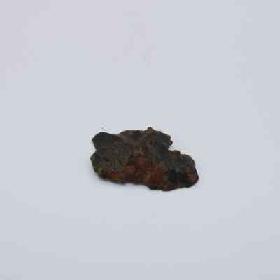 Closeup of basaltic glass flake: A small, dark fragment of basaltic glass flake lies on a plain white background, showcasing rough, uneven textures and a glossy surface.