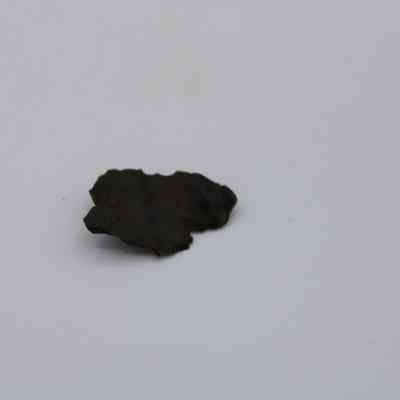 Closeup of basaltic glass flake: A fragmented piece of basaltic glass flake rests gently against a plain, light-colored background, displaying its dark, irregular surface texture.