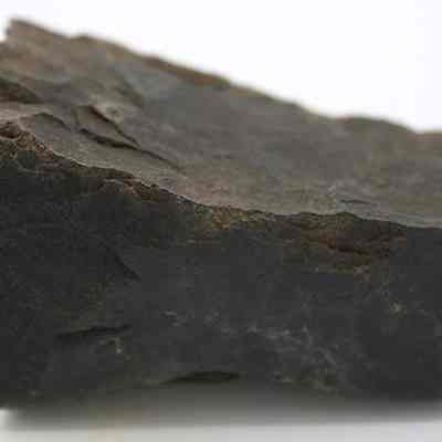 Profile of basalt adze fragment: The image shows a dark, roughly textured adze fragment, with irregular edges, made from stone, against a plain white background.