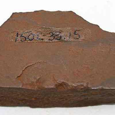 Side of basalt adze fragment with alternate id number visible: The image shows a rugged fragment of an adze with a reference number written in black ink on its surface.
