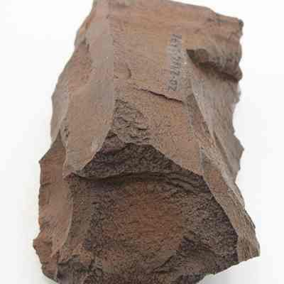 Close up lengthwise view of a basalt adze blank: The image shows a rough, brown stone tool or artifact with sharp edges, resembling an adze blank, displayed against a plain white background.