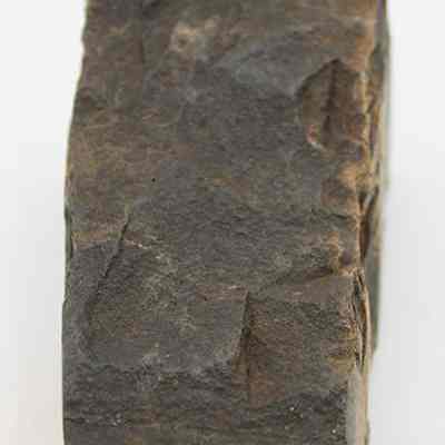 Lengthwise view of basalt adze fragment: The image shows a rugged, dark stone fragment, believed to be part of an ancient adze, featuring a weathered and textured surface.