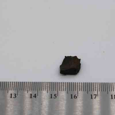 Closeup of tiny glass flake and ruler: A small glass flake is placed beside a metal ruler, highlighting its size with measurements marked in centimeters.