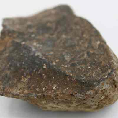 Closeup of basalt scraper: The image displays a rough, irregularly shaped brown and gray rock with a textured surface, showcasing various shades and patterns, placed against a plain white background.