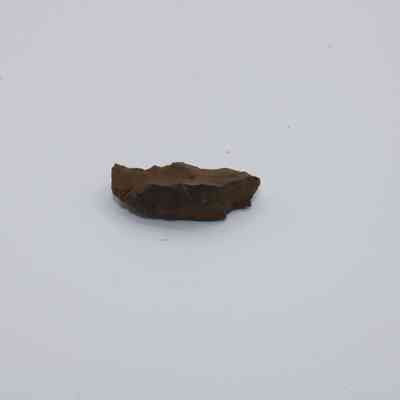 Basaltic glass piece: A small, jagged piece of basaltic glass, dark and irregular, rests against a plain white background, highlighting its natural texture and form.