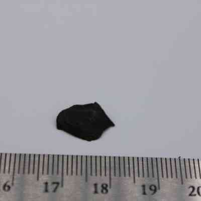 Closeup of basaltic glass flake: The image shows a small basaltic glass flake placed on a white surface, with a ruler nearby for size reference.