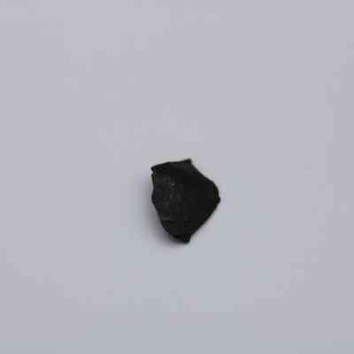 Basaltic glass flake: A small piece of basaltic glass flake lays on a plain white surface, showcasing its dark, smooth texture and irregular shape.