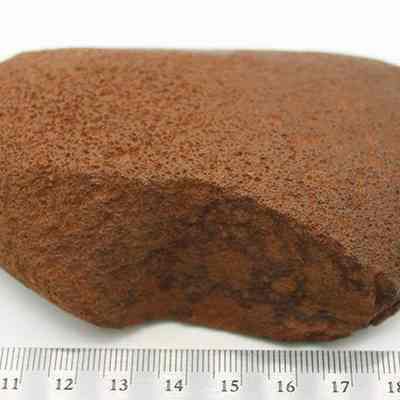Basalt hammerstone with ruler: The image shows a brown, rough-textured hammerstone placed on a flat surface, with a measurement scale beneath it indicating its size.