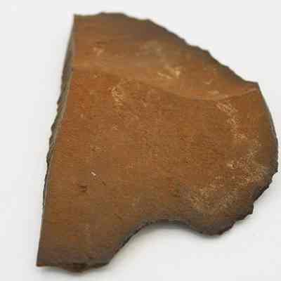 Lengthwise view of possible basalt scraper side: The image shows a rusty, brown-colored, irregularly shaped rock fragment, possibly a scraper, against a white background.
