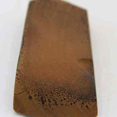 Lengthwise view of basalt adze (ko'i): This image shows a piece of stone that is part of an ancient adze (ko'i), featuring a smooth, polished surface with a slightly rounded edge and dark markings.