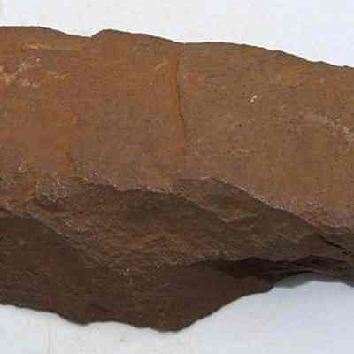 Profile of a basalt adze fragment: The image shows a weathered, brown fragment of an adze, featuring rough, irregular surfaces and edges, possibly indicating its age and historical usage.