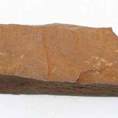 Basalt adze fragment: The image shows a rough, brown stone adze fragment with uneven surfaces and jagged edges, likely used in ancient woodworking or carving.