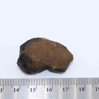 Pāhoehoe (smooth lava) core and metal ruler: A small, irregularly shaped lava core rests beside a ruler, showcasing its rough, dark exterior and measuring approximately 4 centimeters in length.