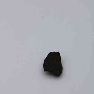 Closeup of basaltic glass flake: The image shows a small, dark basaltic glass flake resting on a plain, light gray surface.