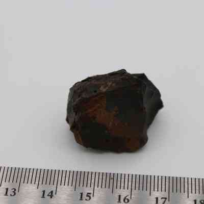 Closup of basaltic glass core with ruler: The image shows a rough, dark basaltic glass core placed next to a ruler for scale, highlighting its irregular shape and textured surface.