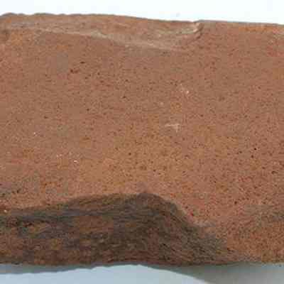Closeup profile of a basalt hammerstone: The image depicts a roughly shaped, reddish-brown hammerstone, displaying signs of wear, likely used as a tool for striking or shaping other materials.
