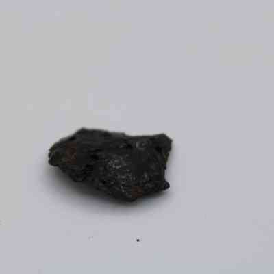Close up of basaltic glass flake: The image shows a small, dark basaltic glass flake with a glossy texture, lying on a neutral grey surface, featuring irregular edges.