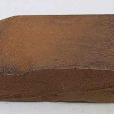Profile of basalt adze (ko'i): The image shows a roughly hewn, brown stone adze (ko'i) head, characterized by its flat, rectangular shape and beveled edge, likely used in shaping.