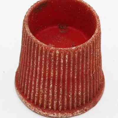 Closeup of plastic cap: The image shows a red, textured cylindrical object with a flared base and vertical grooves, resembling a small cap.