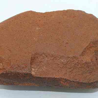 Closeup of a hammerstone: The image depicts a brownish, roughly shaped hammerstone resting on a white surface, showcasing its natural, weathered texture.