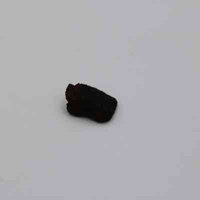 Closeup of basaltic glass core: The image shows a small piece of basaltic glass core resting on a plain white surface, highlighting its dark color and rugged texture.