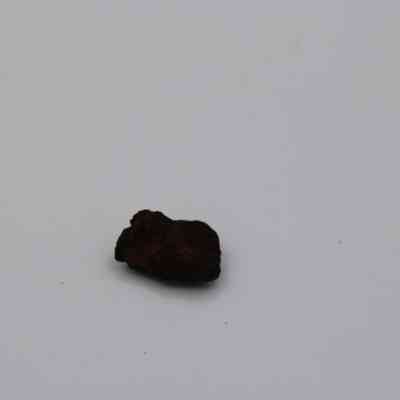 Closeup of basaltic glass core: A small piece of basaltic glass rests on a plain surface, displaying its rough, dark texture and irregular shape.
