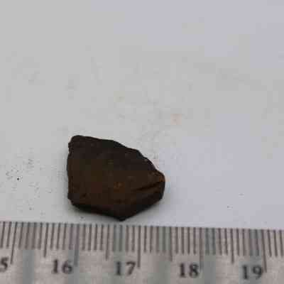 Closeup of basaltic glass flake and ruler: The image shows a small, dark basaltic glass flake on a white surface, next to a metric ruler for scale.