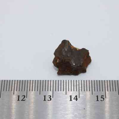 Closeup of basaltic glass core and ruler: A small basaltic glass core is placed against a ruler, highlighting its size and dark, rough textured surface.
