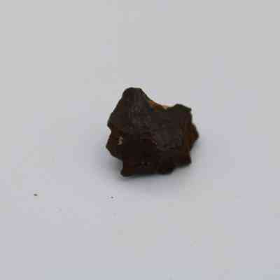 Basaltic glass core closeup: The image shows a dark, irregularly shaped basaltic glass core placed against a plain white background, highlighting its rough texture.