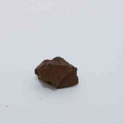 Closeup of basaltic glass core: The image shows a small, irregularly shaped piece of basaltic glass core, resting on a plain, white surface, with a rough texture and dark