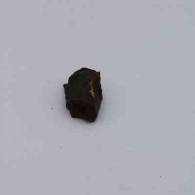 Closeup of basaltic glass core: A small, rough basaltic glass core sits on a plain white surface, showcasing its dark and textured appearance distinctively.