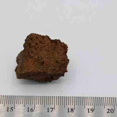 Basaltic glass core with metal ruler: The image shows a rough, brown basaltic glass core with a textured surface, placed beside a ruler for scale.