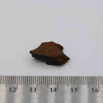 Closeup of basaltic glass core with metal ruler: The image shows a piece of basaltic glass core placed on a surface beside a ruler for scale measurement.