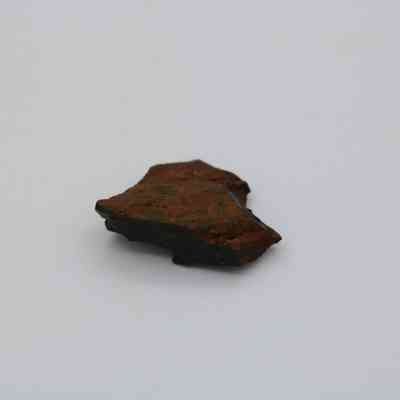 Closeup of basaltic glass core: The image shows a small, brownish basaltic glass core with rough, jagged edges, placed on a light, featureless background.