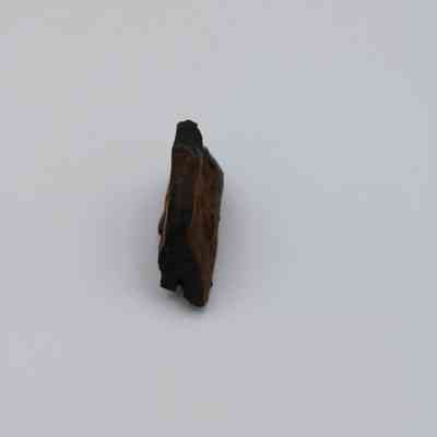 Edge of basaltic glass core: The image shows a small, irregular basaltic glass core with a rough, dark surface, positioned against a neutral background.