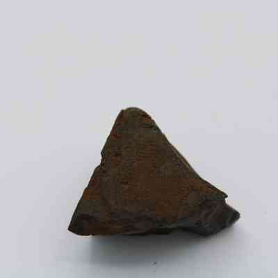 Closeup of a basaltic glass core: The image displays a triangular piece of basaltic glass core with a rough, dark surface, set against a plain, light background.