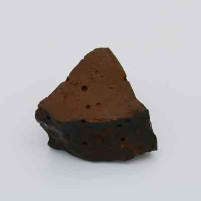 Closeup of basaltic glass core: The image shows a triangular piece of basaltic glass core, displaying a smooth, dark surface with pitted texture.