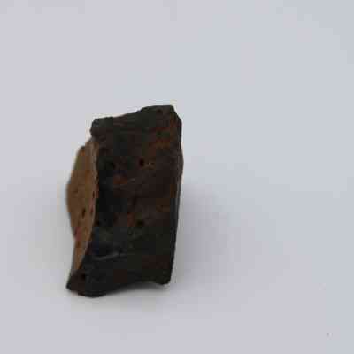 Closeup of basaltic glass core: The image depicts a piece of basaltic glass core, showcasing its rough texture and dark coloration against a plain white background.