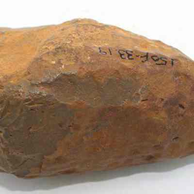 Profile of basalt hammerstone with alternate id number visible: The image shows a stone tool, likely a hammerstone or adze preform, used historically for shaping or crafting, characterized by its irregular surface.
