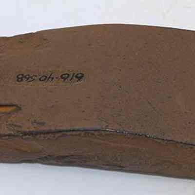 Polished side of basalt adze (ko'i) fragment with alternate id number visible: The image shows a flat, brown adze (ko'i) fragment with a rough surface and visible markings, suggesting it's an ancient archaeological artifact.