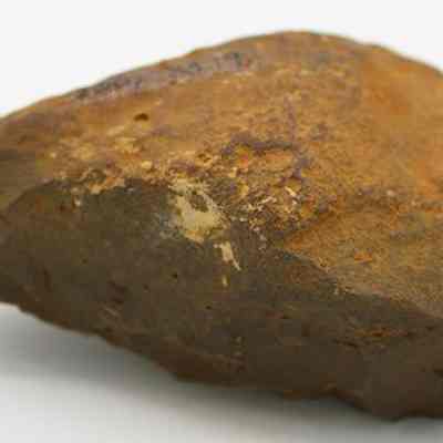 Basalt hammerstone: The image shows a rough, brown stone with a flattened shape, possibly a hammerstone or adze preform, exhibiting weathered surfaces and potential tool use.