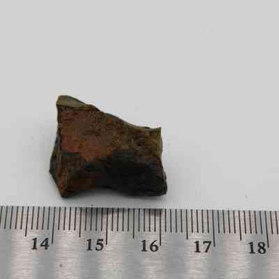 Closeup of basaltic glass core with ruler: The image shows a small piece of basaltic glass core resting on a white surface with a metal ruler for scale.